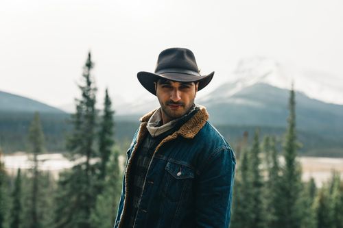 Free A man wearing a cowboy hat stands outdoors against a scenic mountain backdrop in Jasper, Alberta. Stock Photo