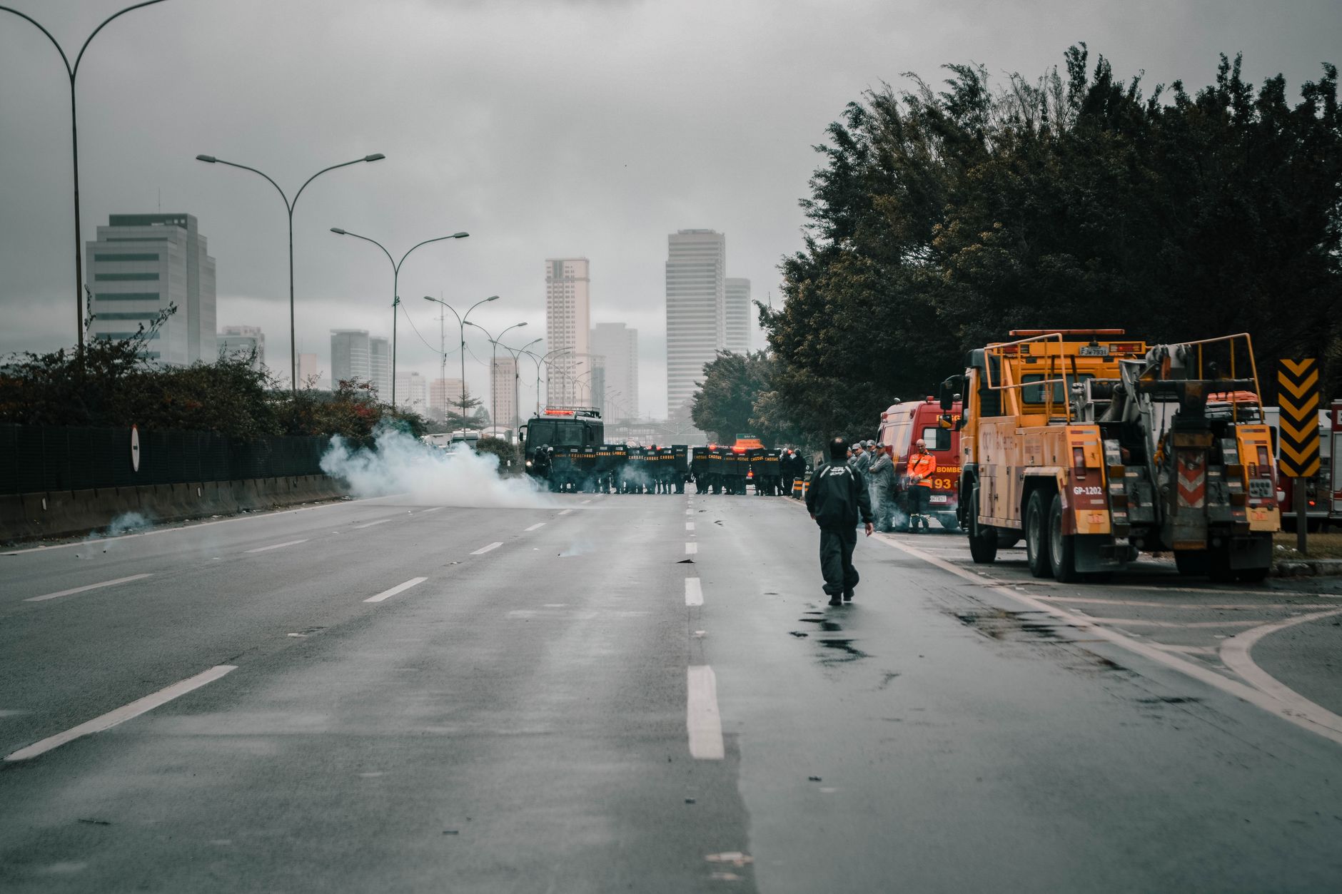 Tense urban scene showing police presence in riot gear amidst smoke during a protest.