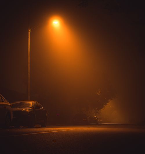 Free A foggy street at night illuminated by a street lamp with parked cars lining the road. Stock Photo