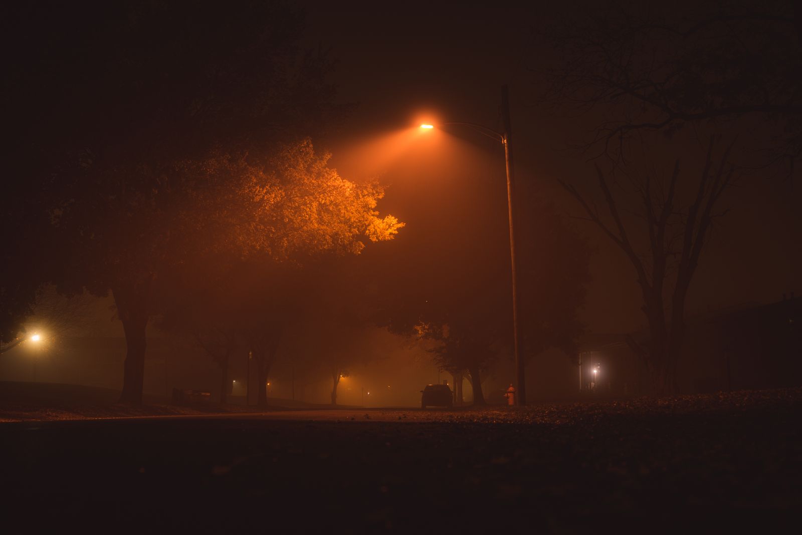 Empty small-town street at night with a single street lamp glowing through fog, illustrative photo