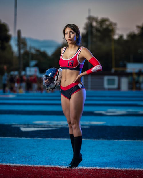 Woman in Red Sports Bra and Black Shorts Running on Blue Field