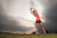 一位女士身着运动服，在戏剧性的日落天空下伸展身体，展现了健康的生活方式