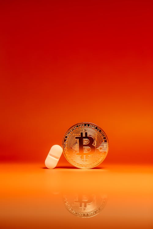 A Bitcoin and a Pill on Orange Surface