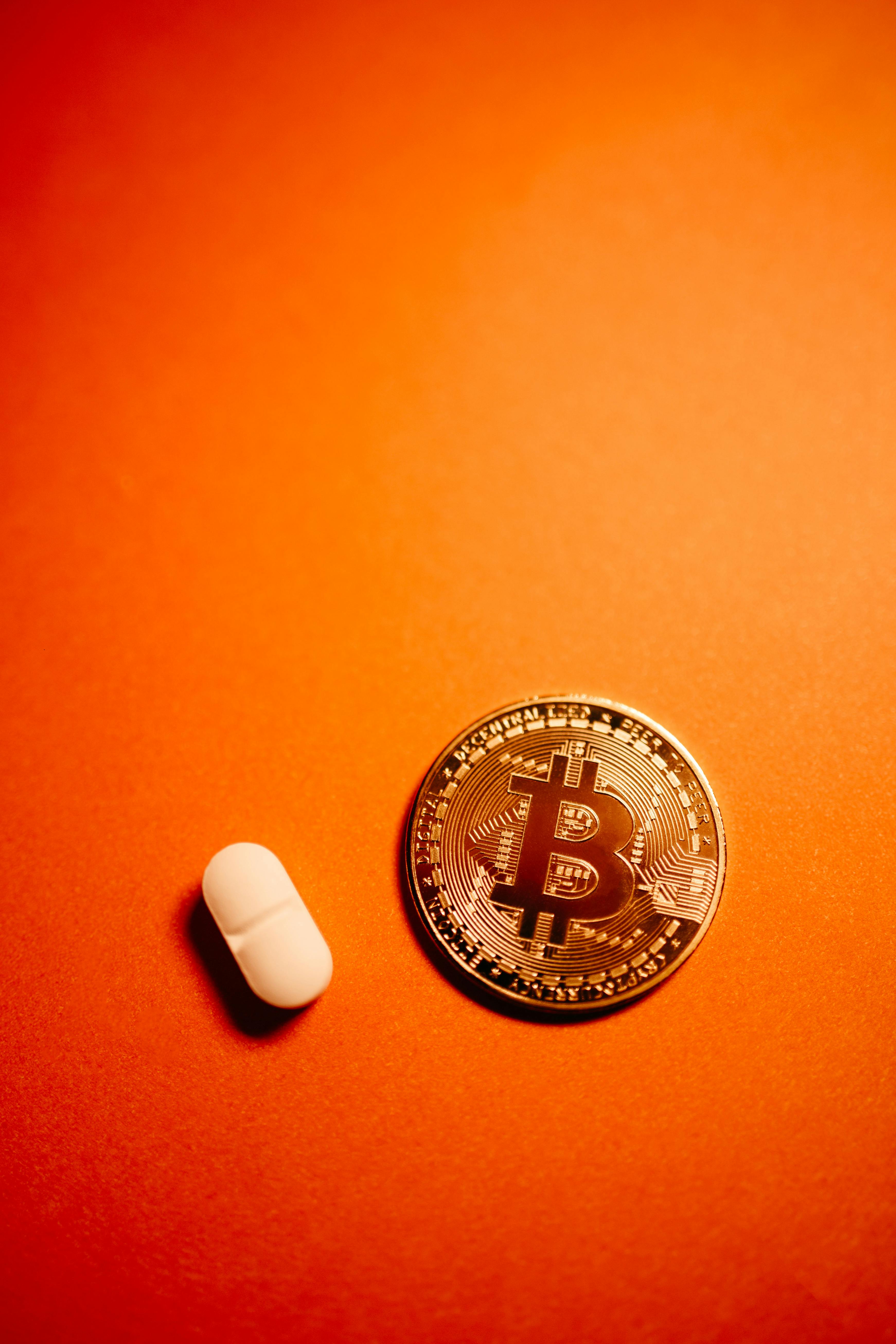 silver bitcoin in orange background beside white pill