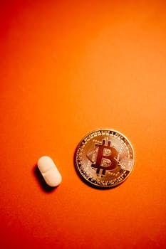 Bitcoin coin next to a pill on an orange background representing finance and health concepts.