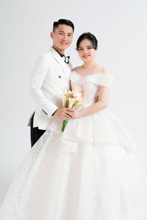 Free A joyful couple in elegant wedding attire poses against a white background. Stock Photo