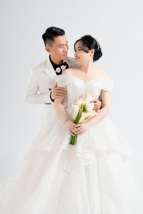 Free Captivating wedding portrait of a loving Asian couple in elegant attire with a white backdrop. Stock Photo