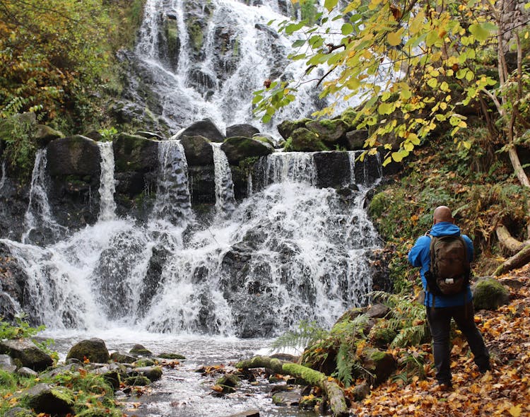 Man Photographing Scenic Waterfall In Mountains