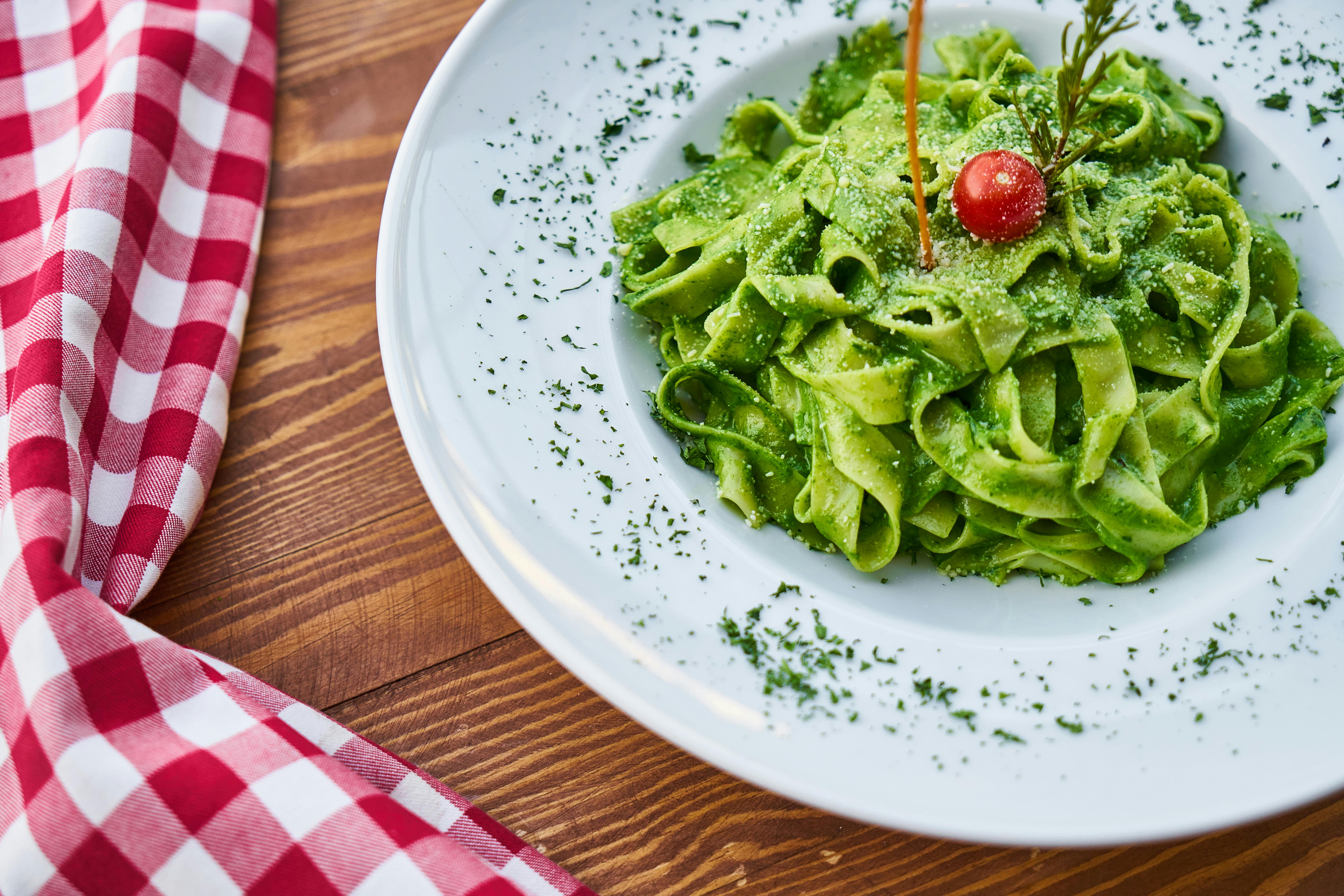 flat pasta noodle with green sauce dish and cherry tomato on top