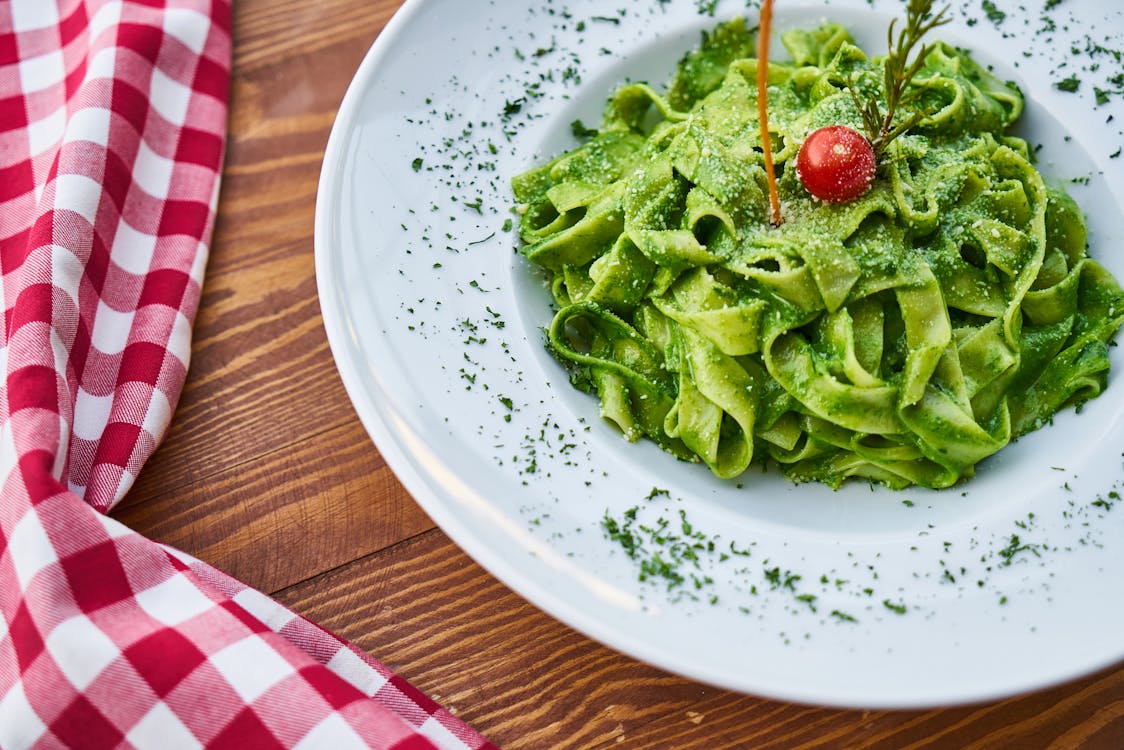 Free Flat Pasta Noodle With Green Sauce Dish and Cherry Tomato on Top Stock Photo