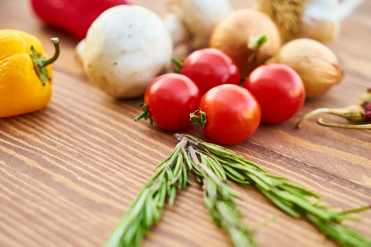 Aneka sayur segar dengan tomat dan rosemary di meja kayu untuk eat clean