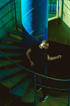 Stylish man descending a spiral staircase, creating dramatic shadows and lighting.