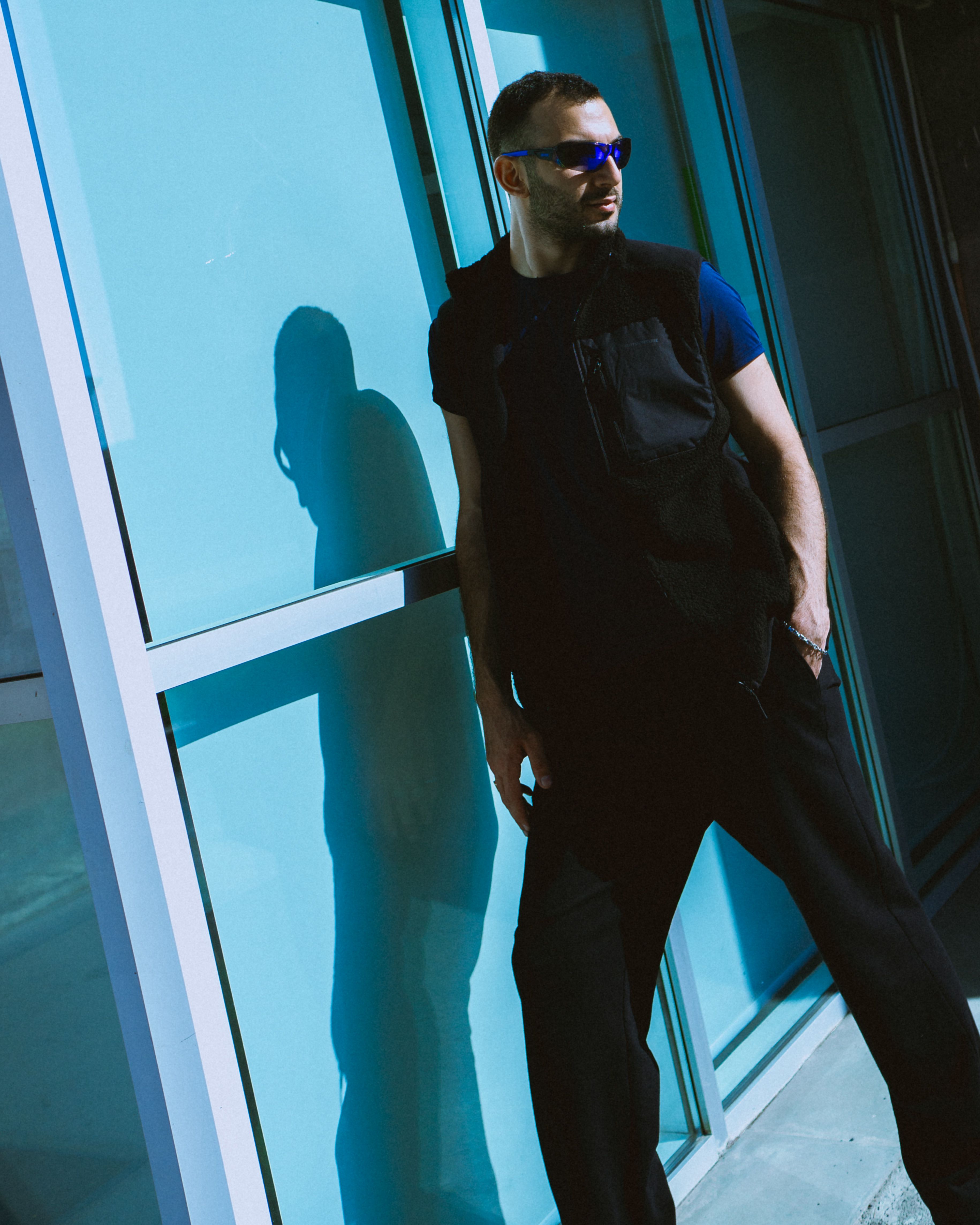 A Man in a Black and Blue Outfit and Sunglasses Posing while Leaning on ...