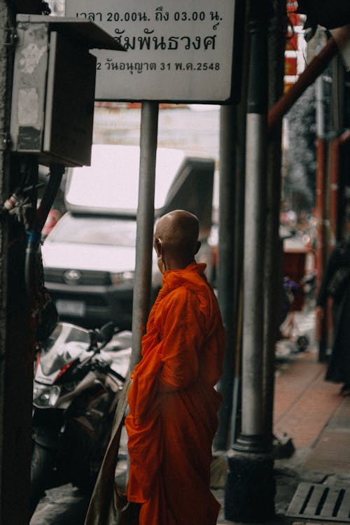 Man in Orange Kasaya Standing Beside a Steel Post