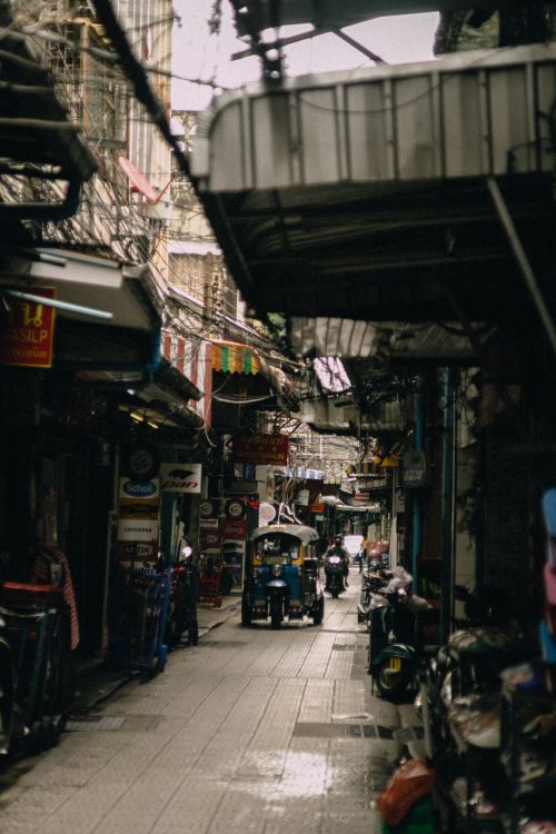 Free A bustling narrow alley marketplace with shops, stalls, and a tuk-tuk in a vibrant downtown setting. Stock Photo