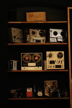 A collection of vintage reel-to-reel tape recorders and audio equipment arranged on shelves.