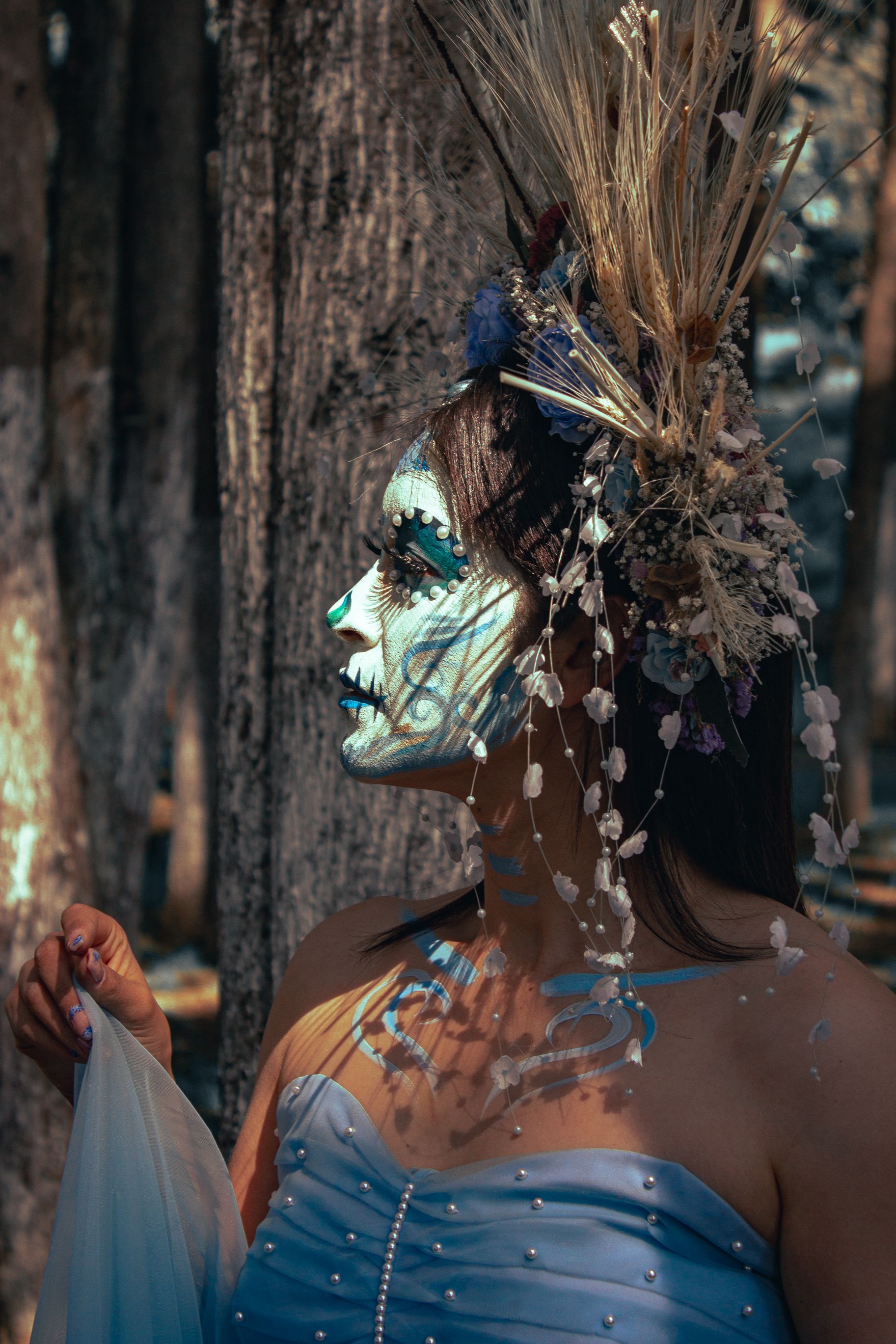A woman in a forest setting, adorned in detailed face paint and elaborate headdress, embodying artistic expression.