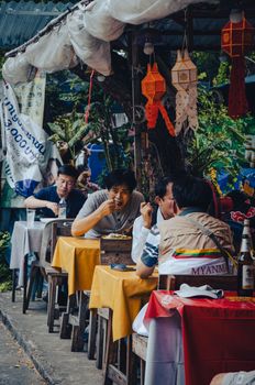 Candid shot of people dining outdoors at a street restaurant adorned with lanterns and local decor.
