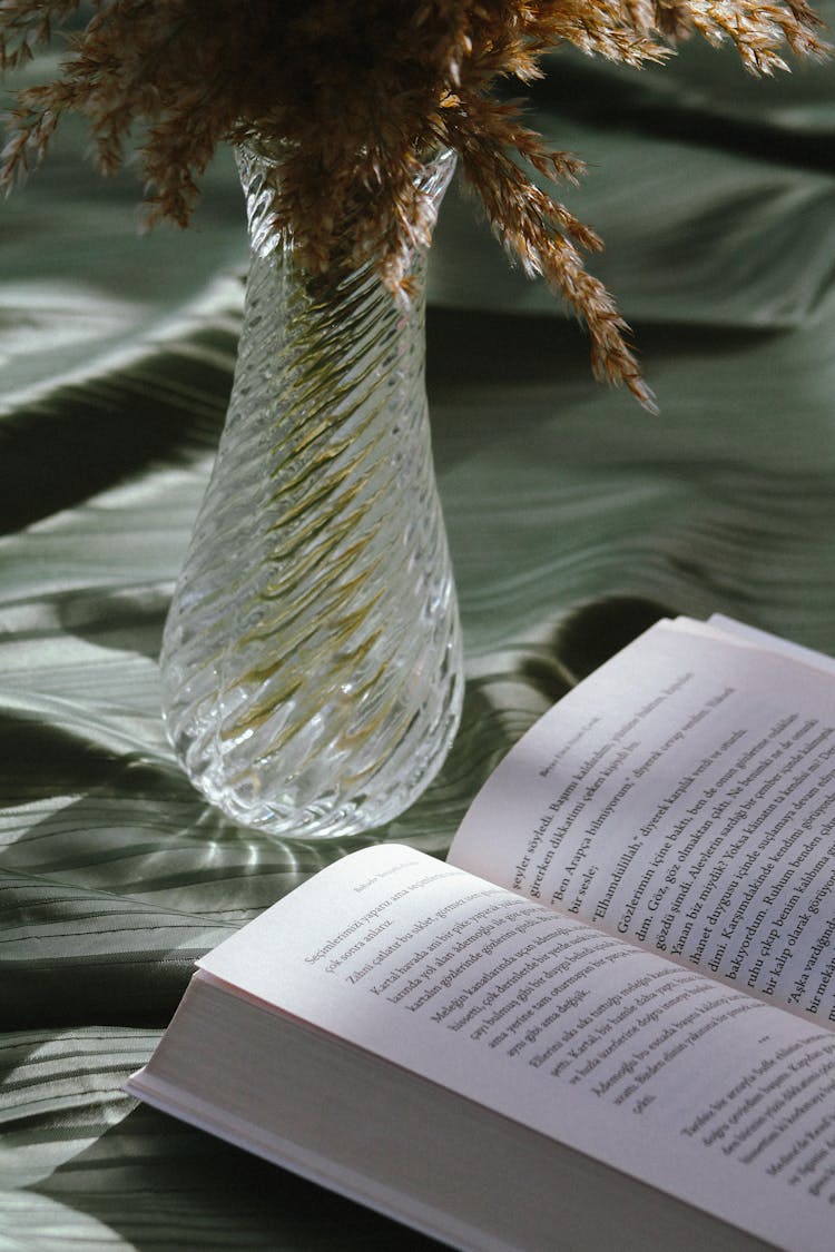 A Glass Vase Near A Book