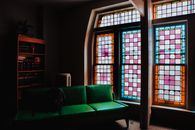 Inviting living room featuring a green couch, bookshelf, and stunning stained glass windows.