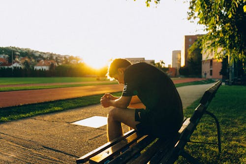 Free Man Sitting on Bench Near Track Field While Sun Is Setting Stock Photo