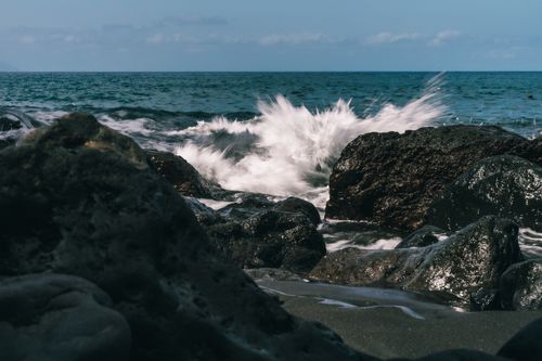 Free Majestic ocean waves crashing against dark rocks under a blue sky. Stock Photo