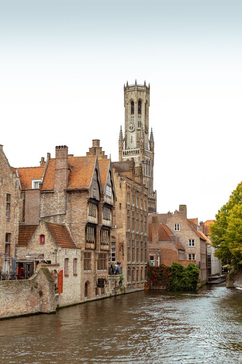 Free Charming view of historic architecture along Bruges canal with tower in background. Stock Photo