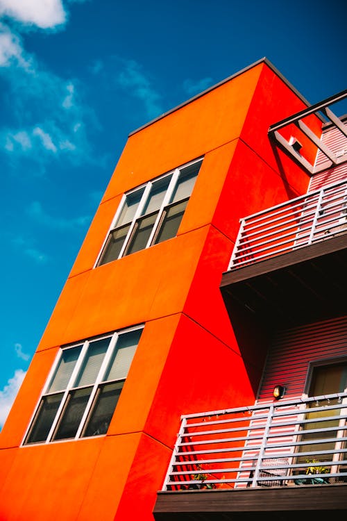 無料 青と白の空の下でオレンジ色のコンクリートの建物のローアングル写真 写真素材