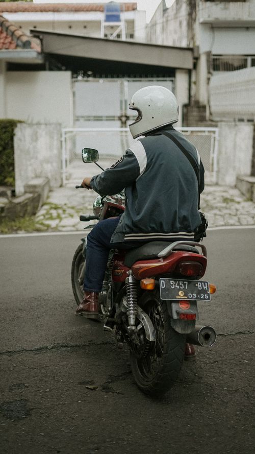 Free A motorcyclist in a helmet riding on a street, captured from behind. Urban setting, casual morning ride. Stock Photo