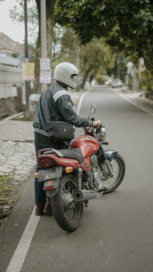 Free Motorcyclist stands beside red motorcycle on a quiet rural road. Stock Photo