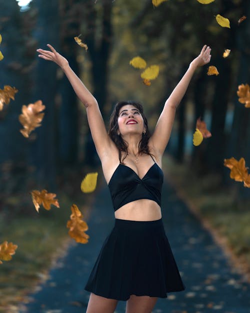 Free Woman in Black Spaghetti Strap Dress Catching Falling Maple Leaves Stock Photo