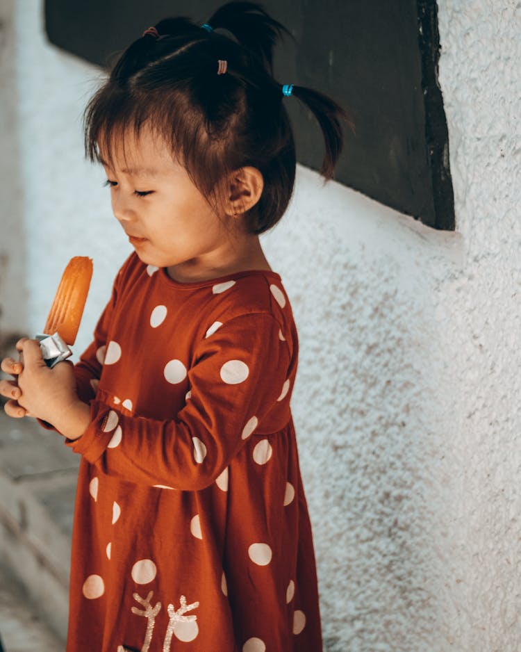 A Kid In A Polka Dot Dress Eating A Popsicle