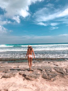 A woman enjoys a sunny day walking along a stunning beach in Bali, Indonesia, with clear skies ahead.