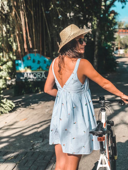 A Woman Wearing Brown Straw Hat is Standing Beside a Bicycle