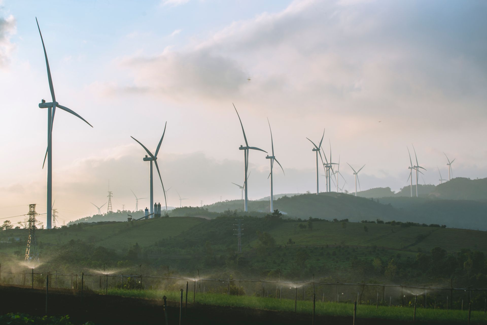 Wind turbines on green hills producing renewable energy under a cloudy sky.