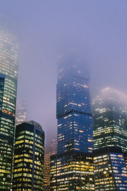Misty evening view of a modern city skyline with illuminated skyscrapers under foggy conditions.