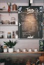 咖啡馆内环境舒适，黑板上写着茶菜单，木架上摆放着杯子和植物