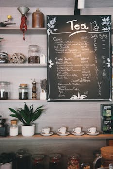 咖啡馆内环境舒适，黑板上写着茶菜单，木架上摆放着杯子和植物