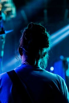 Silhouette of a person with dreadlocks in a nightclub, illuminated by blue stage lights.