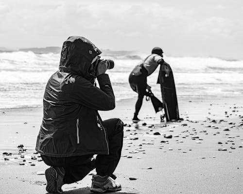 Grayscale Photo of a photographer Taking Picture of a Person Wearing Swimfins on Seashore
