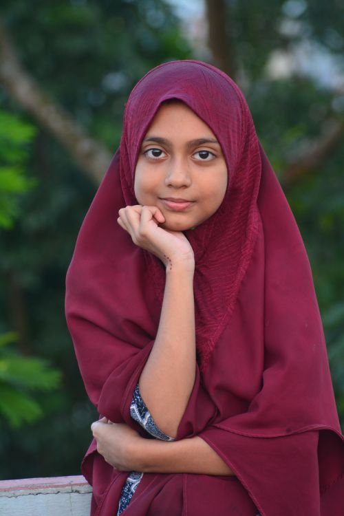 Free A young girl wearing a burgundy hijab poses confidently outdoors, exuding warmth and charm. Stock Photo