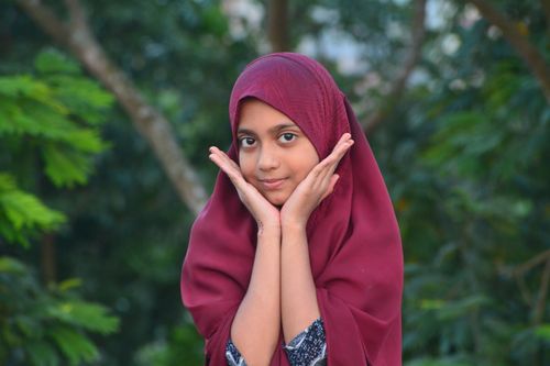 Free Portrait of a young girl wearing a hijab, hands on cheeks, outdoors. Stock Photo