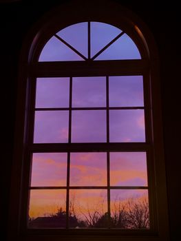 Silhouette of trees against a vibrant purple and orange sunset seen through an arched window.