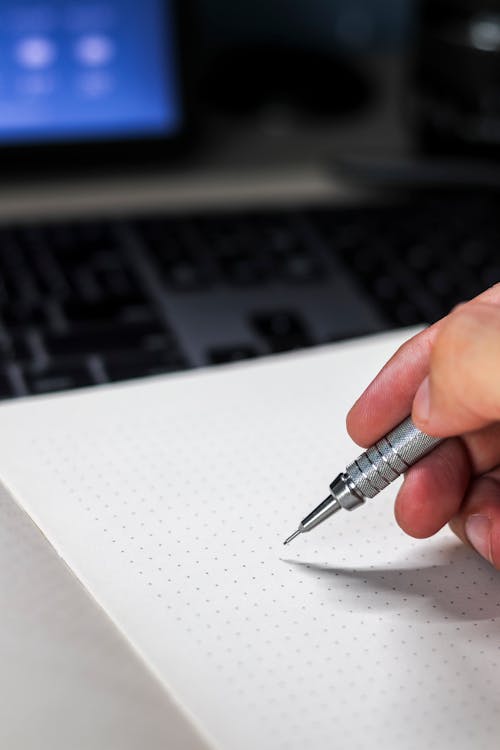 Close-up of a Person Holding a Pen about to Write on an Empty Notebook Page