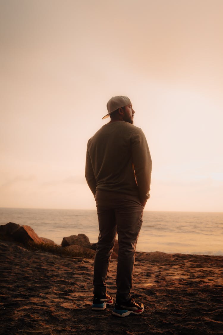 Back View Of Man In Sweatshirt Standing On Sand Near Sea