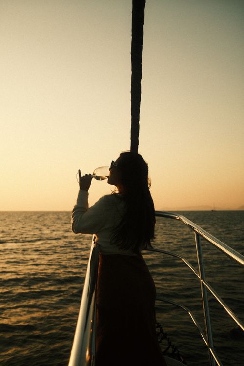 Free Silhouette of a woman drinking wine on a yacht's deck at sunset, against a serene sea backdrop. Stock Photo