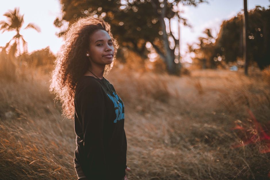 A young woman with curly hair enjoys the fall sunset in a natural setting.