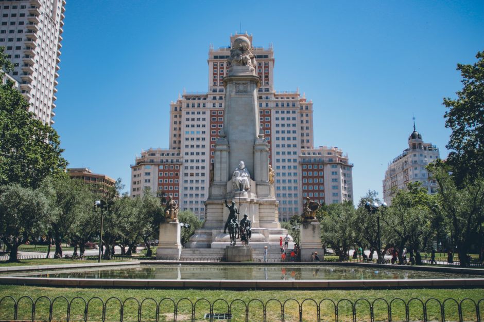 Vista de la estatua monumental en la Plaza de España, Madrid, rodeada de edificios modernos y vegetación.