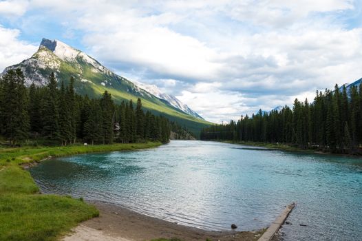 Breathtaking view of a serene lake surrounded by evergreen trees and majestic mountains under a cloudy sky.