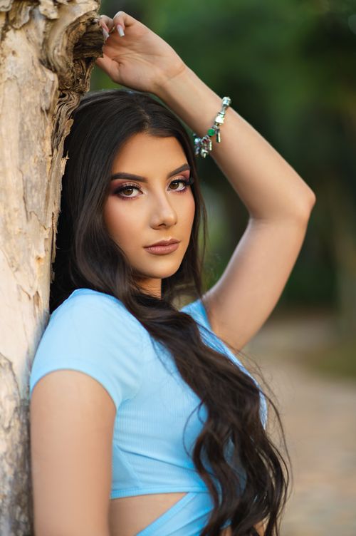 Free Portrait of a woman in a blue dress posing elegantly by a tree in a serene outdoor setting. Stock Photo